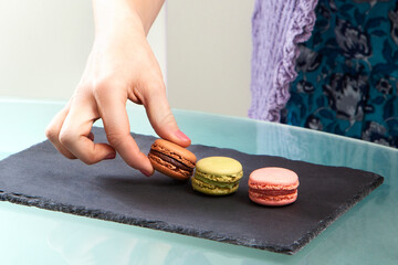 3 macarons, brown, green and pink, presented on a culinary blackboard. young woman's hand catching...