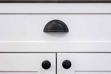 Photograph of a matte black drawer cup pull handle on a white cabinet.