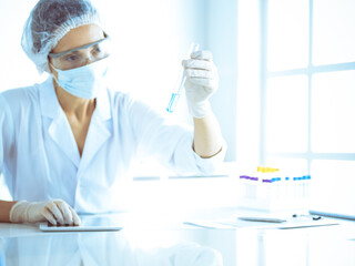 Professional female scientist in protective eyeglasses researching tube with reagents in laboratory toned in blue. Concepts of medicine and science researching