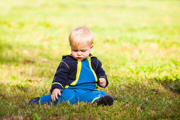 the sad baby is sitting on the lawn looking at the grass