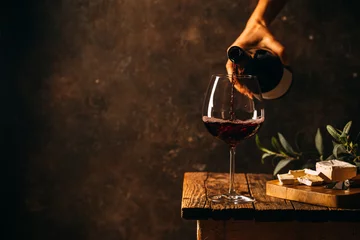 Fotobehang Pouring red wine into the glass against rustic dark wooden background © petrrgoskov