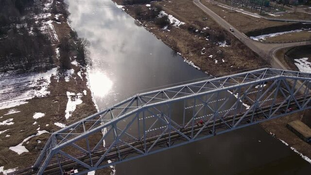 Metal railway train bridge over the river
Belarus Orsha Dnieper River. 
early spring Aerial footage from drone departing away from the bridge revealing landscape