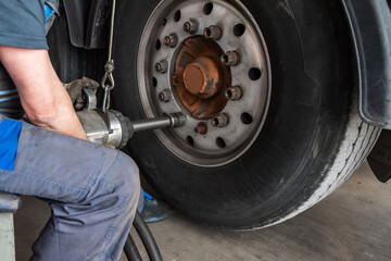 Tire workshop operator removing the lug nuts from a truck wheel with a pneumatic machine.