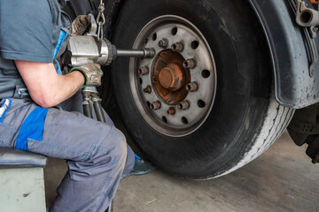 Tire workshop operator removing the lug nuts from a truck wheel with a pneumatic machine.