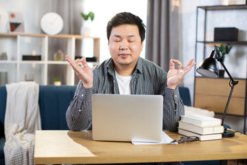 Relaxed young asian man meditating at workplace