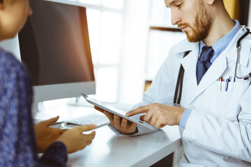 Friendly male doctor and patient woman discussing current health examination while sitting in sunny...