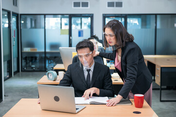 Serious asian female executive consulting with male colleague working with laptop at desk in modern office