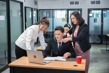 Asian female manager consulting and collaborating with colleagues working with laptop at desk in the office