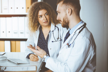 Red-bearded doctor with female colleague discussing current disease therapy while sitting at...