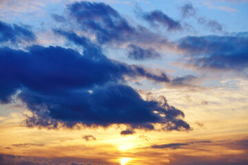 Dark cloud in orange sunset. Dramatic sunset with clouds on the sky. Bright sunlight through the blue sky at sunset or evening time.
