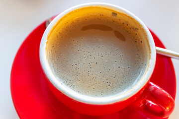 Red cup of hot coffee on white table, top view.