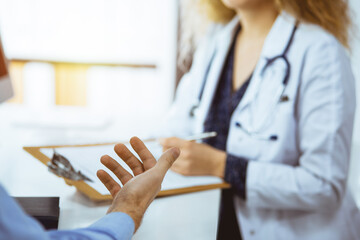 Female doctor and patient discussing current health examination while sitting in sunny clinic,...