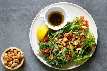 Kale and rocket green salad with cashew nut. Homemade dressing olive oil, balsamic vinegar, salt, black pepper and lemon. Healthy and easy meal. Top view on black table blackground. 