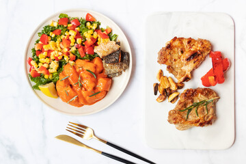 Fresh salmon toss spicy gochujang sauce with healthy green salad kale, corn and tomato on plate with grilled pork steak on marble plate, top view.  