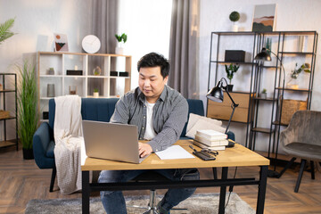 Handsome young Asian man freelancer typing on laptop while working at home