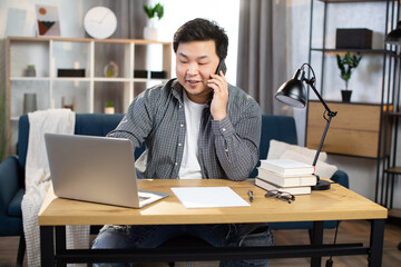 Asian man typing on laptop and talking on mobile