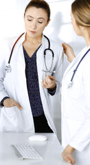 Two female physicians are discussing medical therapy, while standing at the table in a sunny clinic office. Doctors at work. Teamwork in medicine