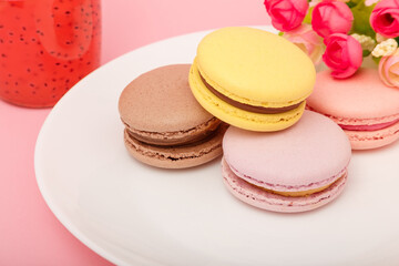 Plate of macaroons on pink background with flowers. Drink in bottle. Sweet pastry, baked products, sweets, dessert. Unhealthy diet.