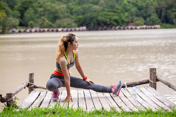 Asian woman athlete warms up with headphones on the waterfront.