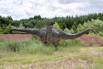 Fototapeta premium A model of a prehistoric dinosaur made available to visitors to a Jurassic park to learn about the history of many millions of years. In the background, vegetation and terrain resembling the natural h
