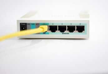 Network cable is plugged into router. Yellow cable in Wi-Fi router. White router with power cord. Router rear view with connections.