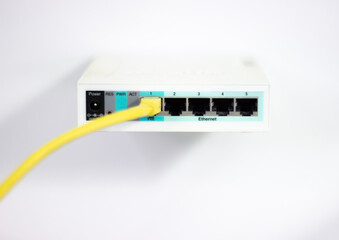 Network cable is plugged into router. Yellow cable in Wi-Fi router. White router with power cord. Router rear view with connections.