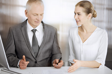 Elderly businessman and woman sitting and communicating in sunny office. Adult business people or lawyers working together as a partners and colleagues at meeting