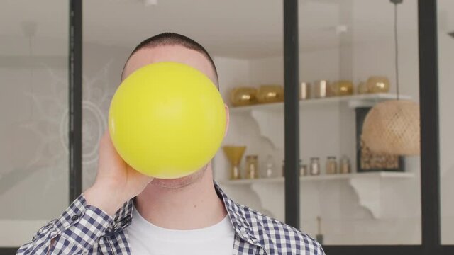 close up in profile young white dark-haired man and inflates yellow ball at home
