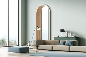 Modern living room interior with arch, mint color on wall and panoramic windows, hills view. Beige sofa with light blue cushions, coffee table, light green chest of drawers and lamp. Parquet floor.
