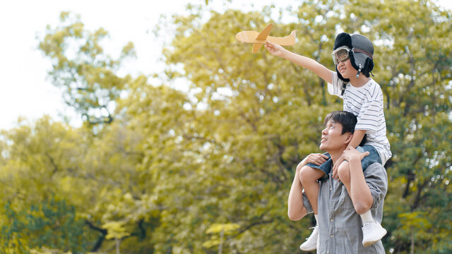 Lifestyle Asian family Father and son sat on his shoulders and run in  park. Paper plane as a toy in hand of kid And there are many big trees in garden Is natural in the morning of summer
