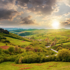 Fototapeta na wymiar carpathian countryside in spring at sunset. beautiful rural landscape in mountain. wet grassy meadow in evening light. road winding through valley to village. distant ridge in the clouds