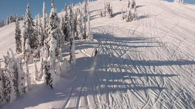 Drone shot of a snowmobile on the snow in the mountains of Revelstoke, Canada.