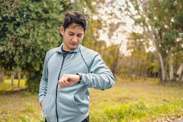Naklejka na ściany i meble Happy sport man in earphone listen music standing and looking at smartwatch during training and running in the park.