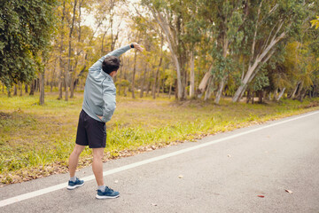 young man stretching in the park before running. Young man workout before fitness training at the park. Healthy and exercise young man warming up on the road beside the forest.