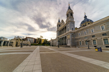 Almudena Cathedral in Madrid and its huge esplanade in front with lampposts and blue sky.
