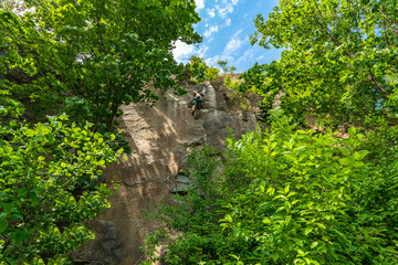 Woman climber with climbing gear equipment climbs on rock wall. Canyon rocks in green forest