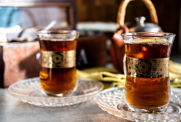 Tea in glass Turkish cups with a gold pattern. A ceramic teapot on a kitchen napkin and a wooden tea box.