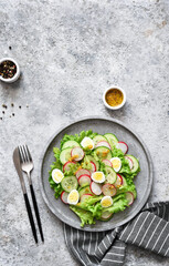 Spring salad with radish, cucumber, egg and salad leaves on a concrete plate.