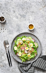 Spring salad with radish, cucumber, egg and salad leaves on a concrete plate.