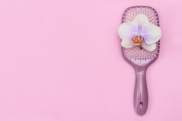 Massage hair brush with orchid flower on pink background, flat lay, copy space.