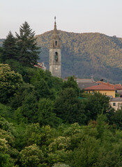 Obraz premium The bell tower of the temple is surrounded by houses and dense vegetation against the backdrop of mountains.