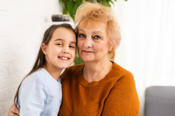 Granny and granddaughter are using a laptop and smiling while sitting on sofa at home