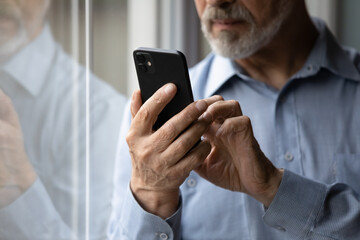 Obraz na płótnie Canvas Aged cellphone user. Close up of mature elderly grey bearded casual male hold modern smartphone device in hands text message online use app. Old man retiree surf web chat make call on cell. Copyspace