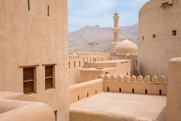 Minaret, dome and walls of medievel arabian fort of Nizwa, Oman. Hot day in arabian desert city. Middle east military architecture.