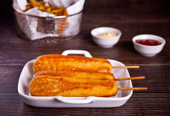 Corndogs on a stick with ketchup and mustard on the wooden table.
