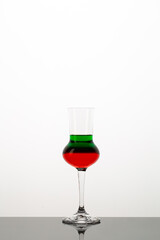Green and red cocktail in the glass for grappa with reflection on white background.Close up of colored alcohol shot with copy space.