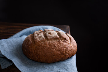 Round rye loaf of bread on a wooden table on a black background, rustic style, home cooking.