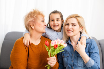 Fototapeta na wymiar Photo portrait of granddaughter congratulating granny giving tulips bunch sitting near mom