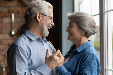 Do you remember our first dance. Loving aged spouses dancing at kitchen celebrate anniversary of strong happy marriage. Elderly man woman in love have romantic date at home move by slow lyrical music