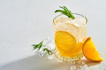 Orange juice or cocktail with rosemary and orange with ice in glass, cold summer lemonade on light gray slate, stone or concrete background. Beach concept with deep sun shadow. Top view. - obrazy, fototapety, plakaty